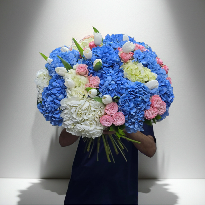Bouquet of blue, pink, and white flowers held by a person against a plain background