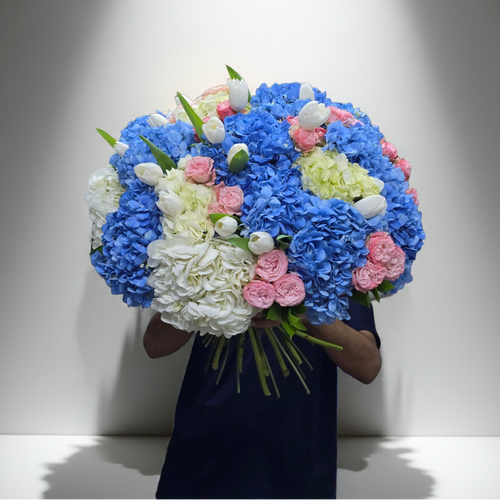 Bouquet of blue, pink, and white flowers held by a person against a plain background